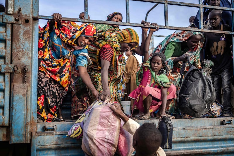 Sudanese refugees carry their belongings as they get off a lorry loaded with families arriving at the transit centre