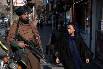 A Taliban fighter stands guard as a woman walks past in Kabul. AP