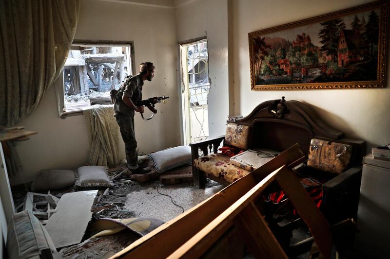 FILE - In this July 27, 2017 file photo, a U.S.-backed Syrian Democratic Forces fighter looks through a window as he takes his position inside a destroyed apartment on the front line, in Raqqa, Syria. Amnesty International, an international rights group, urged the U.S.-led military coalition battling the Islamic State group to investigate airstrikes that killed civilians in the campaign to liberate the Syrian city of Raqqa from the extremists. Amnesty said Tuesday, Aug. 7, 2018,  that the U.S.-coalition's admission last month that it killed 78 more civilians than previously reported in the 2017 assault on Raqqa was just the "tip of the iceberg." (AP Photo/Hussein Malla, File)