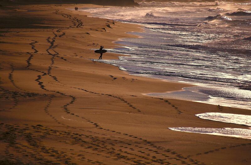 People walk along the beach as a surfer holding his board looks at the waves on Merewether Beach in Newcastle, located north of Sydney, Australia. David Gray/Reuters