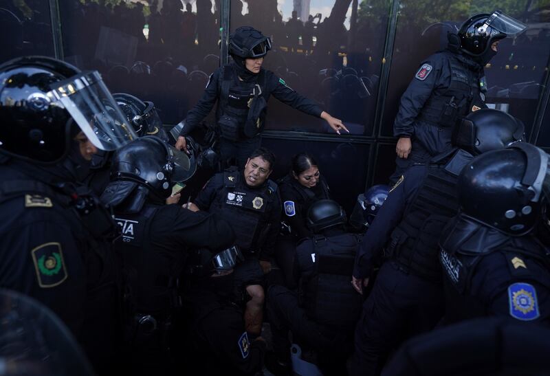 Police officers lean against a protection barrier in pain, surrounded by fellow officers, after being wounded by an explosive device thrown by protesters during clashes outside the attorney general's office, in Mexico City.  The demonstrators were marching to mark the anniversary of the 2014 disappearance of 43 students of a teachers’ college in Iguala, Guerrero. AP