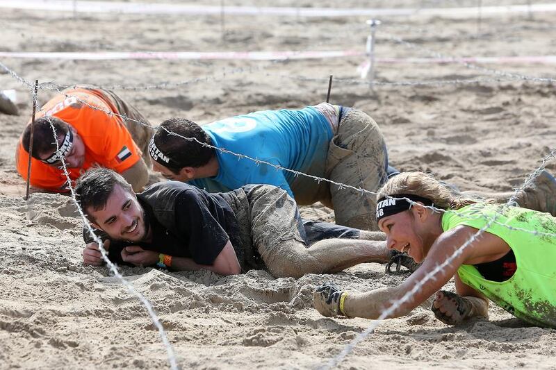 A man smiles as a he encourages a female competitor under the barbed wire.
