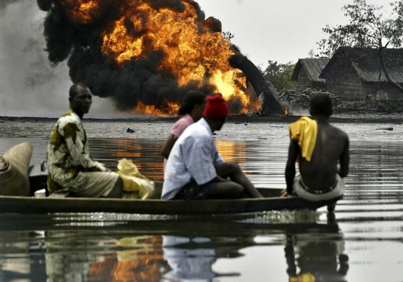 In this 2005 file photo, people evacuate their homes by boat as they pass smoke and flames billowing from a burning oil pipeline belonging to Shell, across the Opobo Channel in the Niger Delta community of Asagba Okwan Asarama. On Wednesday, the company agreed to pay a Nigerian fishing community Dh305.9m for the worst oil spill ever suffered in the country. George Osodi, File/AP Photo