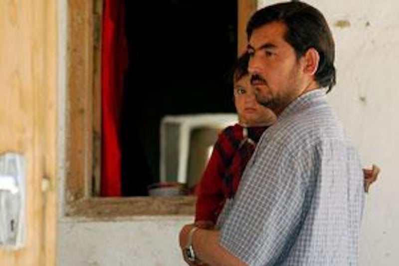 Aminullah holds his daughter in his home where his pregnant wife died in a gun battle.