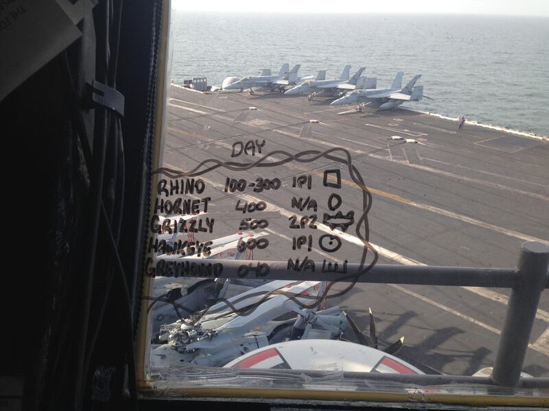 A view of the USS George HW Bush’s flight deck from inside the Primary Flight Control room. The Flight Control team takes note of what goes on on the flight deck by scribbling on the windows in marker pen.