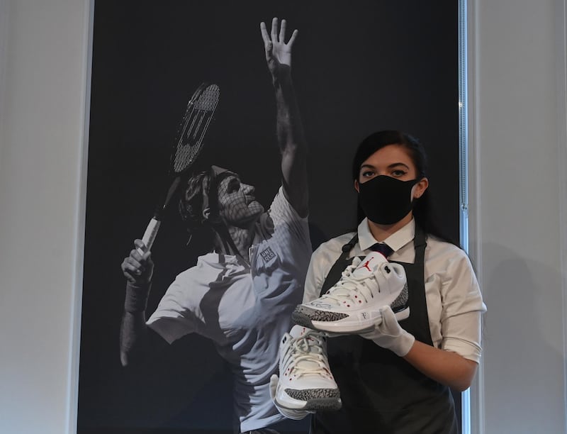 A Christie's employee poses with Swiss tennis champion Roger Federer's Nike Air Jordans shoes from the 2014 US Open at the Christie's auction house, in London.