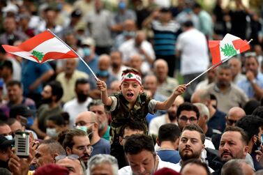A boy wears military-style camouflage khakis and waves two Lebanese national flags at an anti-government protest. EPA