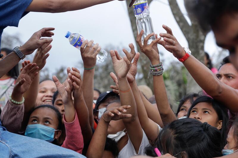 Residents scramble to grab bottled water given by a passing citizen at a town near Taal volcano, Tagaytay, Cavite province, southern Philippines on Sunday Jan.19, 2020. Many poor families living near Taal volcano have been affected due to loss of income after business closures in the area, Philippine officials said Sunday the government will no longer allow villagers to return to a crater-studded island where an erupting Taal volcano lies, warning that living there would be "like having a gun pointed at you." (AP Photo/Aaron Favila)