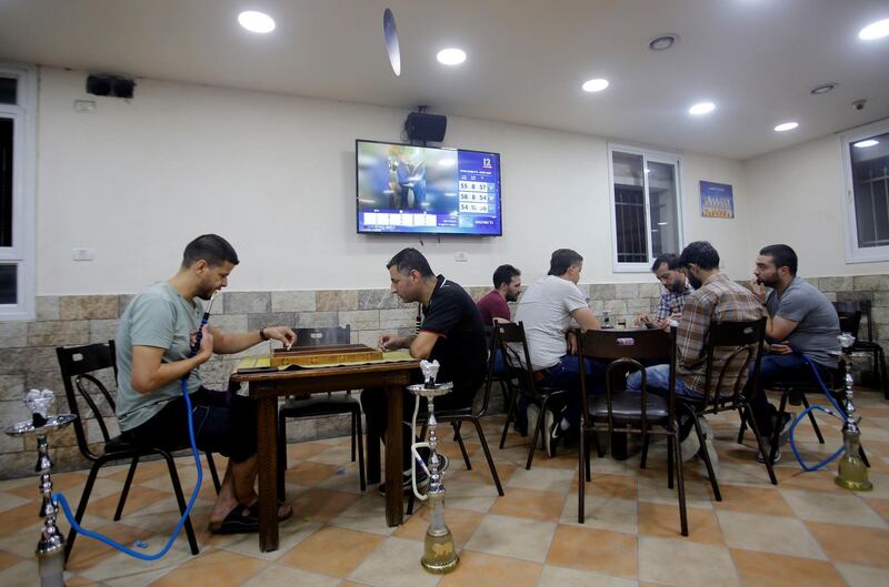 Palestinians play a board game and cards as television screen displays news about the results of the Israel's parliamentary election, in a coffee shop in Hebron in the Israeli-occupied West Bank. REUTERS
