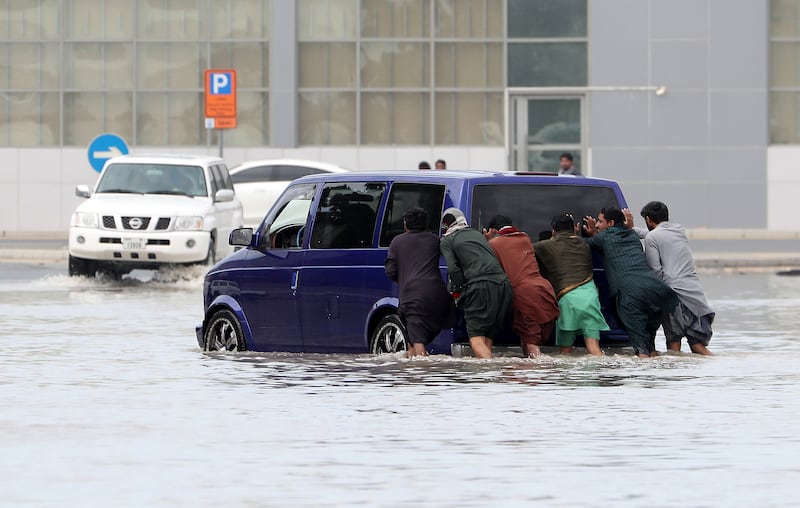 Workers push a car stranded on a flooded street in Al Quoz Industrial area. Pawan Singh / The National