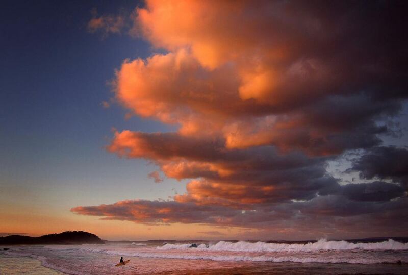 A surfer holding her board wades through the surf as clouds above are lit by the setting sun at Mollymook Beach on the south coast of New South Wales. David Gray / Reuters