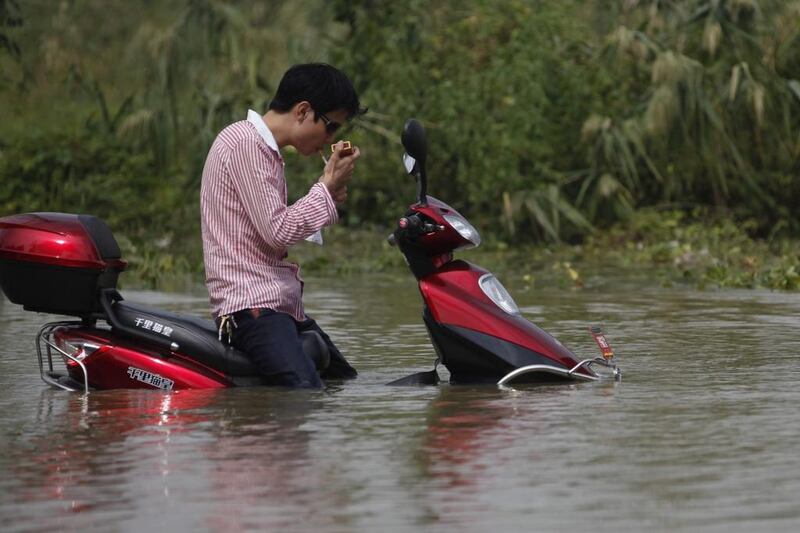 A man on a scooter lights a cigarette on a flooded road in Tongxiang City in east China. EPA