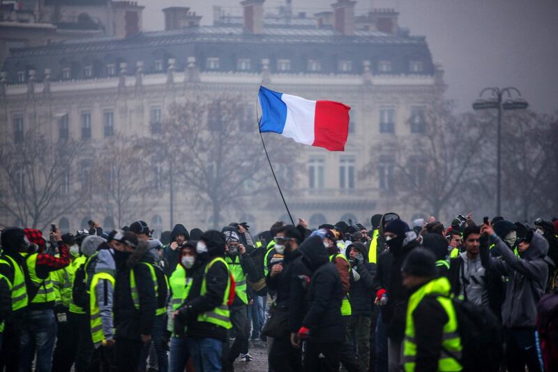 TOPSHOT - Demonstrators gather near the Arc de Triomphe as a French flag floats during a protest of Yellow vests (Gilets jaunes) against rising oil prices and living costs, on December 1, 2018 in Paris.  Anti-government protesters torched dozens of cars and set fire to storefronts during daylong clashes with riot police across central Paris on December 1, as thousands took part in fresh "yellow vest" protests against high fuel taxes. / AFP / -

