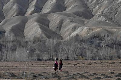 Hazara women walk while carrying buckets on their head on the outskirts of Bamiyan province on March 7, 2021. / AFP / WAKIL KOHSAR
