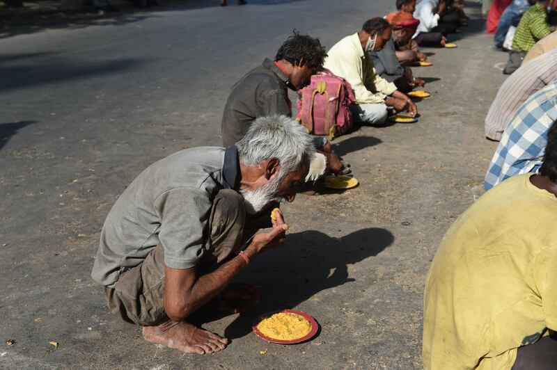 Poor and homeless people eat plates of 'khichdi' (Indian dish made from rice and lentils) distributed by volunteers on a street in Ahmedabad on May 30, 2020. (Photo by SAM PANTHAKY / AFP)