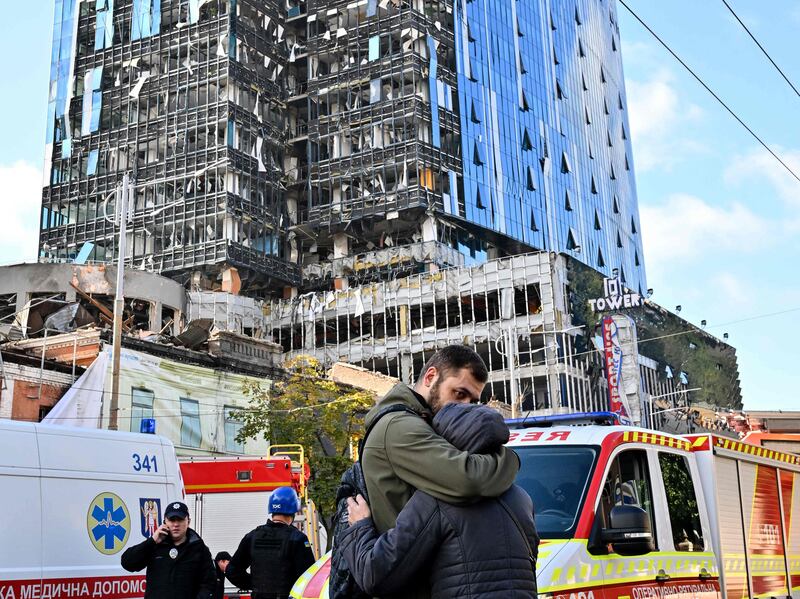People comfort each other outside a partially destroyed multi-storey office building after several Russian strikes hit the Ukrainian capital of Kyiv. AFP