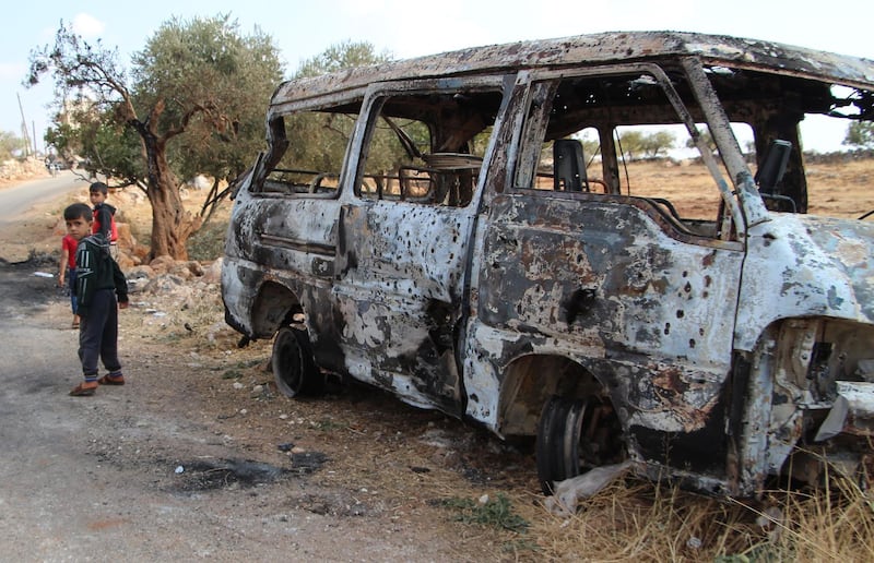 Syrian children walk past a damaged van at the site of helicopter gunfire which reportedly killed nine people near the north-western Syrian village of Barisha. AFP