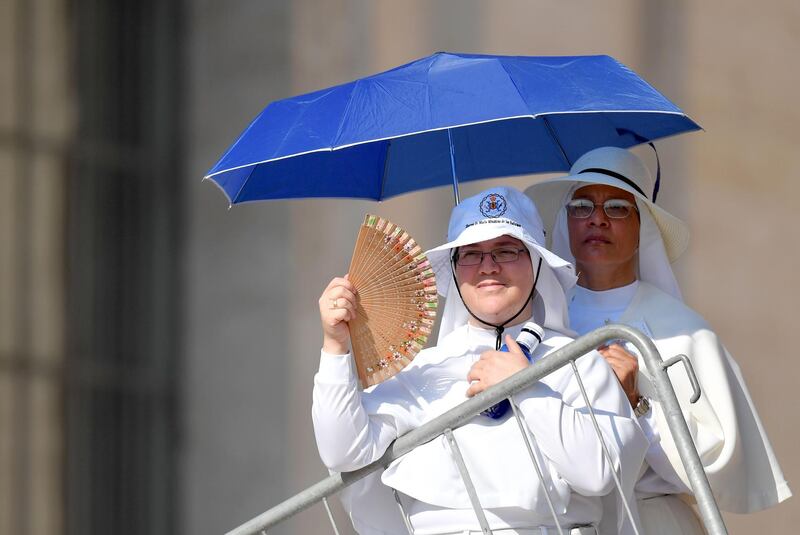 Nuns stand in the shadow of an umbrella and use a fan to protect from the heat on a hot summer day before attending the Pope's weekly general audience at Saint Peter's square at the Vatican.  AFP