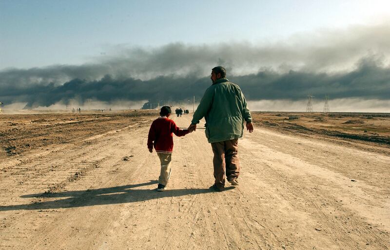 March 29, 2003: A man and child walk on a road near the entrance of the besieged city of Basra as oil fires burn in the distance. Baath Party loyalists take up positions in Basra, Iraq's second largest city, making it a target of the US-led war on Iraq. Getty 