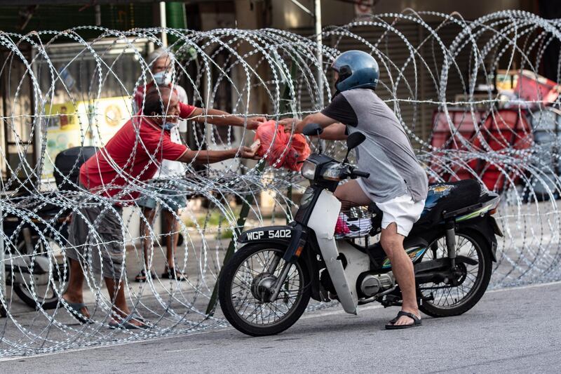A resident receives food supply from a motorist through a barbed wire fence in Petaling Jaya outside Kuala Lumpur, Malaysia. The area was locked down after 15 people were diagnosed with Covid-19.  EPA