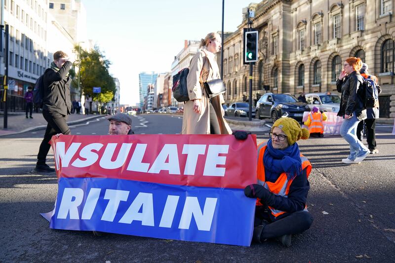 Pedestrians cross the road behind Insulate Britain protesters in Birmingham.