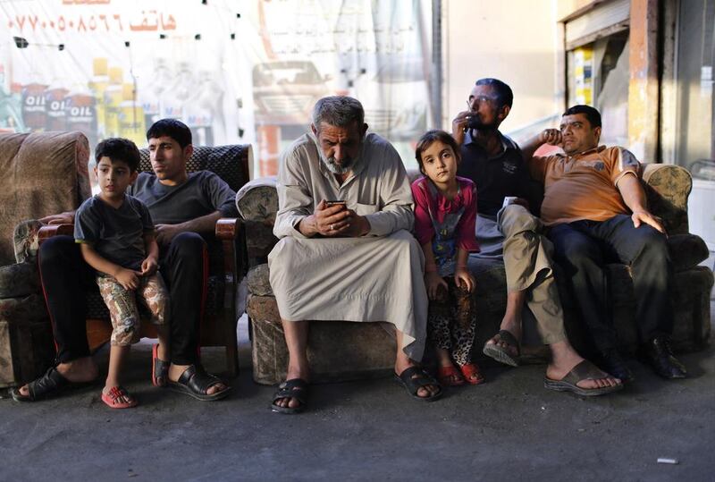 An Iraqi Shi’ite man, center, uses his phone as he sits at an outdoor cafe in Sadr City.
