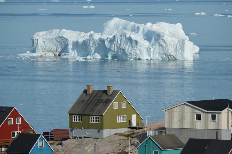 An iceberg floats in Disko Bay behind houses during unseasonably warm weather in Ilulissat, Greenland.   Getty