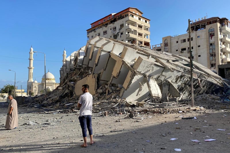 Palestinians stand next to the remains of a tower building which was destroyed in Israeli air strikes, in Gaza City. Reuters