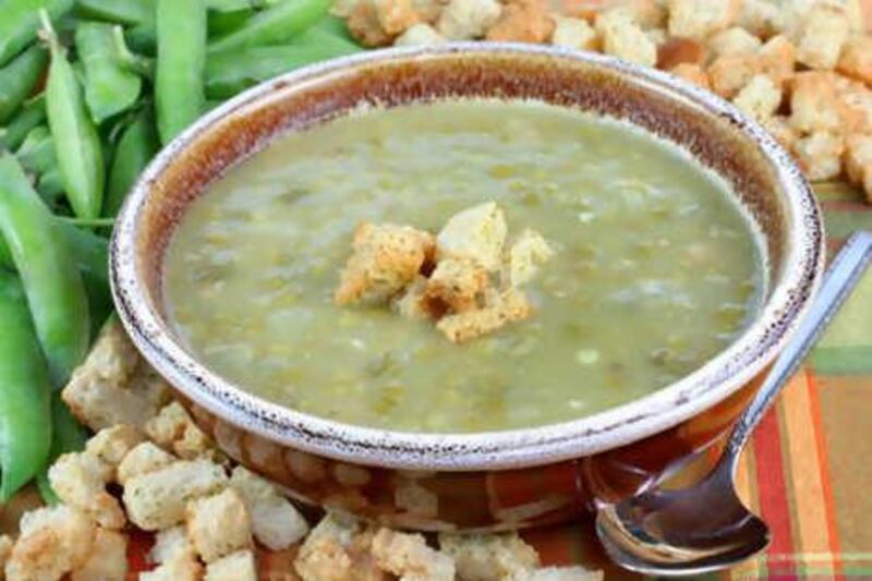 Pea soup in a country bowl surrounded by fresh peas and croutons.