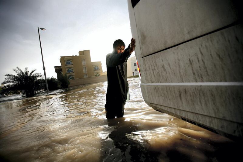 December 13, 2009 / Abu Dhabi / (Rich-Joseph Facun / The National) A man helps a bus driver push his vehicle through a flooded street in Al Bateen after it stalled during the storm, Sunday, December 13, 2009 in Abu Dhabi.  *** Local Caption ***  rjf-1213-rain009.jpg