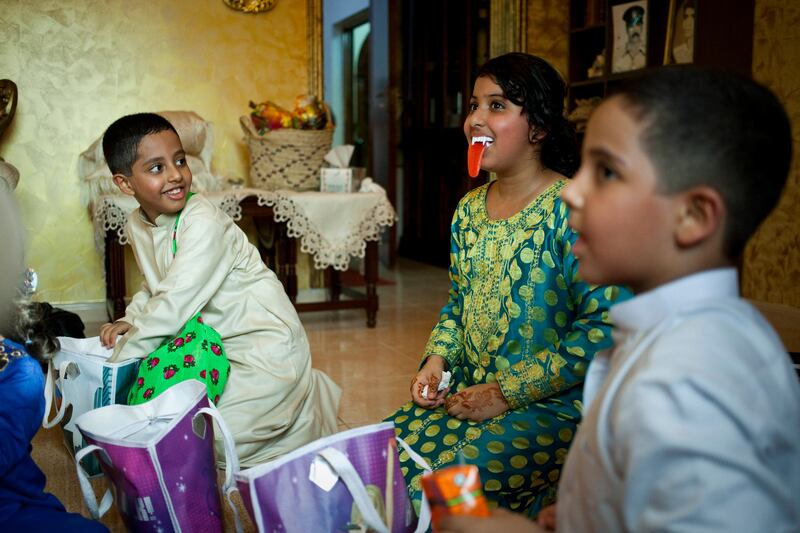 Sharjah, United Arab Emirates - June 23 2013 - Aisha Al Suwaidi, 12, (center) jokes around with her family after opening her two bags filled with sweets and crisps. She has just participated in Hag El Leila, an Emirati tradition that occurs every year 15 days before the start of the month of Ramadan. The tradition involves children walking from door-to-door singing and collecting sweets and money.  (L-R) Her cousins Zayed Al Jabri, 8, and Ahmed Al Jabri, 9, laugh along. (Razan Alzayani / The National)  FOR RYM GHAZAL STORY  *** Local Caption ***  RA0623_hag_el_layla_016.jpg
