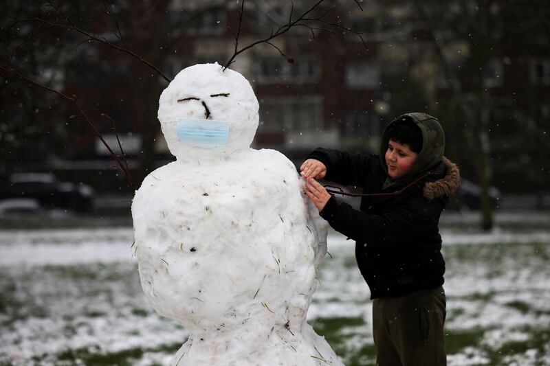 A boy works on a mask-clad snowman on Primrose hill during snowfall in London, Britain. Reuters