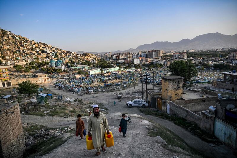 People carry drinking water as they walk along a hillside near the Kart-e-Sakhi cemetery in Kabul. AFP