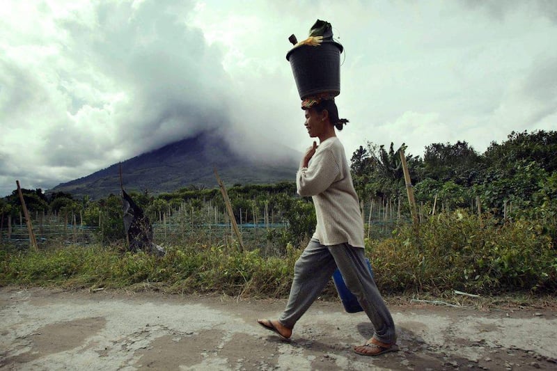 An Indonesian villager walks with a bucket on her head as Mount Sinabung spews volcanic smoke in Kuta Tonggal village, Karo, Northern Sumatra, Indonesia. Dedi Sahputra / EPA