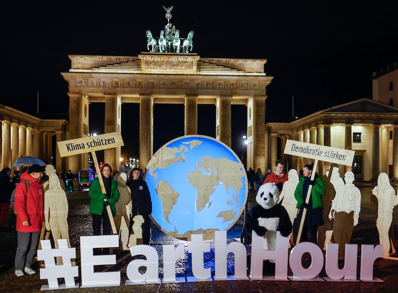 Activists stand in front of the Brandenburg Gate, a moment prior the switch off of the illumination, to mark Earth Hour in Berlin, Germany, 23 March 2024.  Earth Hour takes place worldwide at 8. 30 p. m.  local time and is a global call to cut emissions by switching off lights for 60 minutes to raise awareness of the fight against global climatic change.  The signs read 'protect climate' (L) and 'strengthen democracy'.   EPA / HANNIBAL HANSCHKE