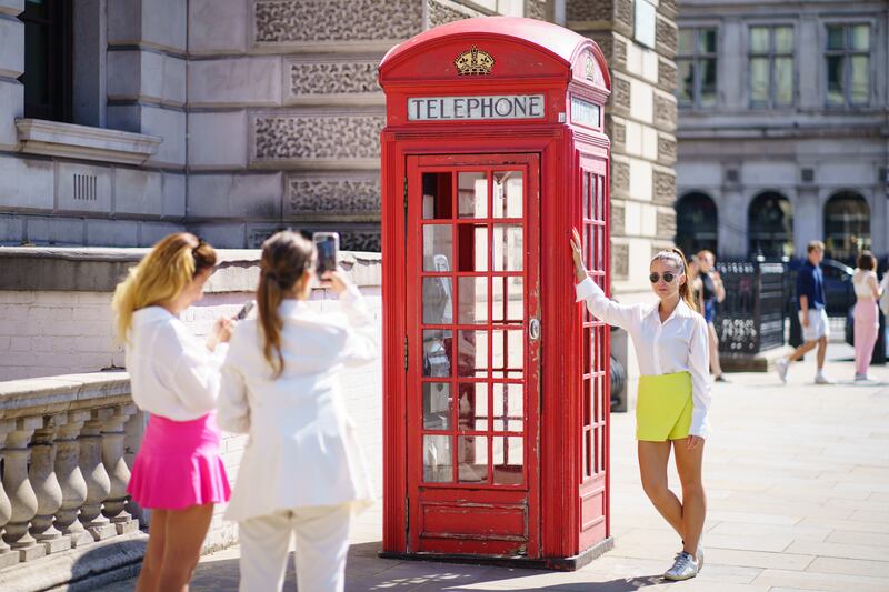 Striking a sunny pose with a London phone box. A tourist enjoys the heat. PA