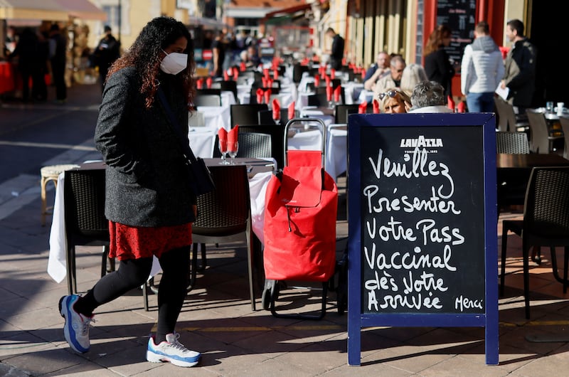 A woman wearing a face mask walks past a sign asking for a vaccine pass outside a restaurant in Nice, France. Reuters