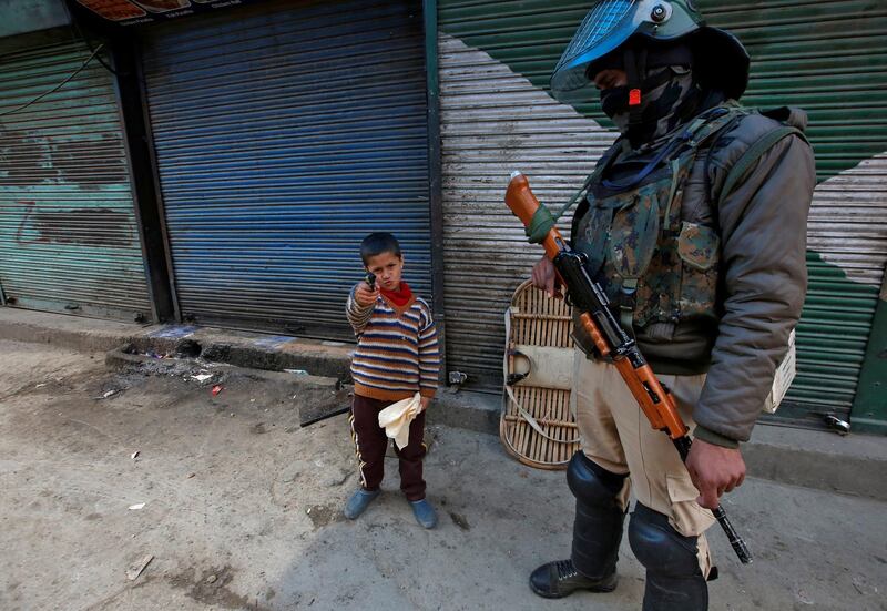 A boy plays with his toy pistol next to an Indian policeman standing guard in front of closed shops during a strike called by Kashmiri separatists against the arrest of Yasin Malik, Chairman of Jammu Kashmir Liberation Front in Srinagar. Reuters