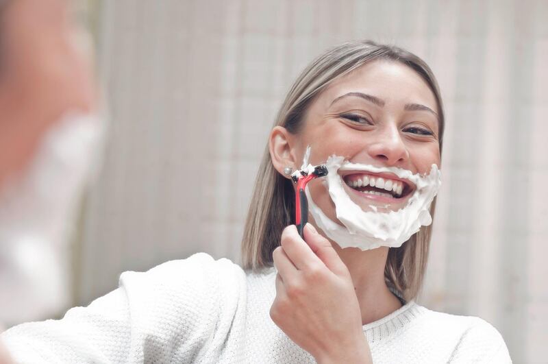 Young smiling woman shaving at the mirror.