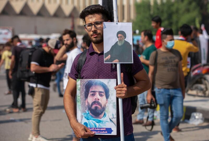 An Iraqi demonstrator lifts placards depicting Shiite cleric Grand Ayatollah Ali Sistani and slain activist Safaa Al Sarai, as protesters gather near the local administration building in the southern city of Basra. AFP