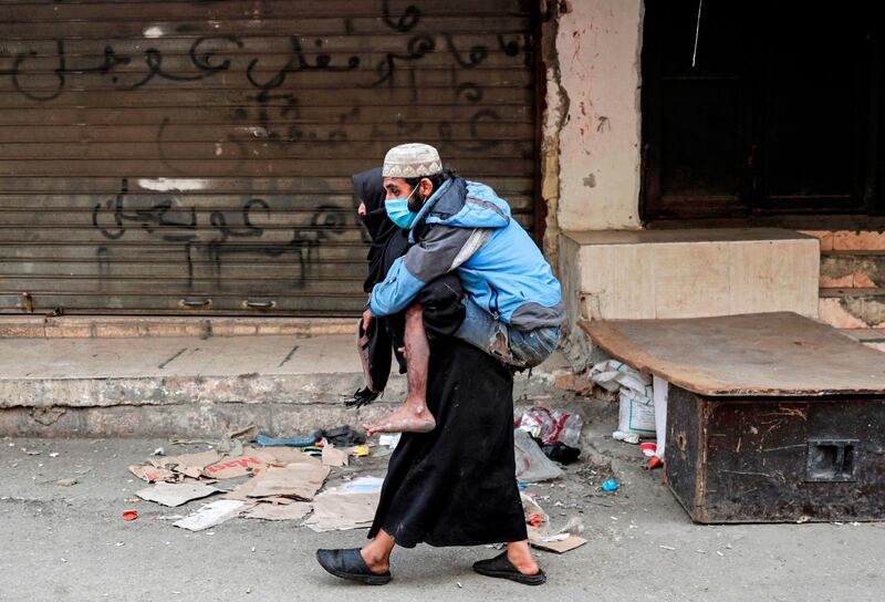 A woman carries a diabled man wearing a protective face mask in the market of the Palestinian refugee camp of Sabra, south of the capital Beirut.  AFP