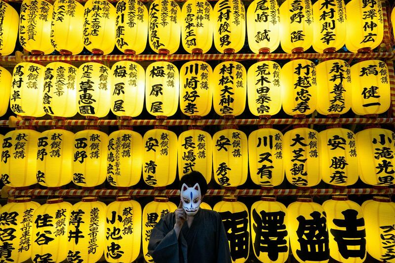 A man a summer kimono poses with a mask as thousands of lanterns are lit up during the Mitama festival at Yasukuni Shrine in Tokyo. AP