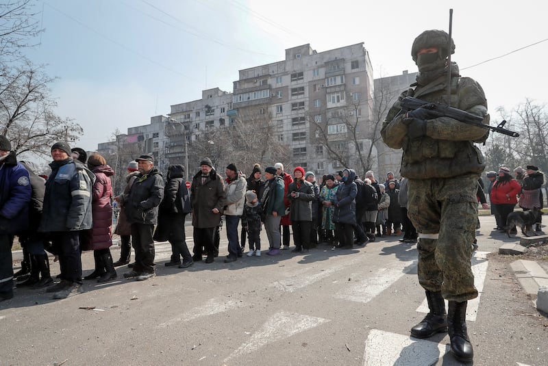 A Russian army soldier stands next to local residents who queue for humanitarian aid delivered during the Ukraine-Russia conflict, in the besieged southern port of Mariupol, Ukraine. Reuters