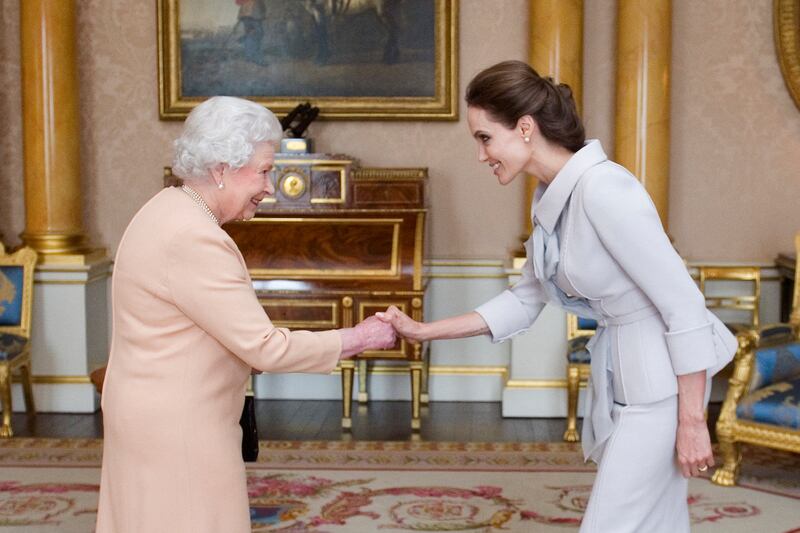 US actress Angelina Jolie curtsies to Queen Elizabeth II on being presented with the Insignia of an Honorary Dame Grand Cross of the Most Distinguished Order of St Michael and St George, at Buckingham Palace in London, on October 10, 2014. AFP
