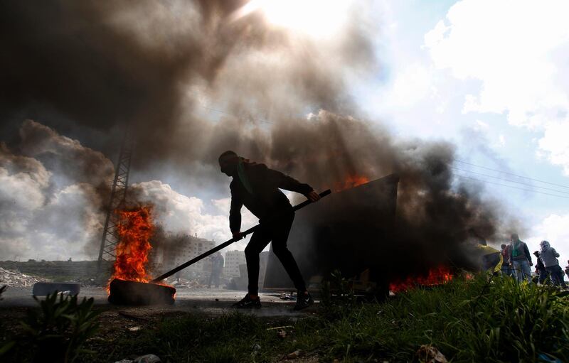 A Palestinian protester burns a tyre during a clashes with Israeli troops at checkpoint Bet El near the West Bank city of Ramallah. AP Photo