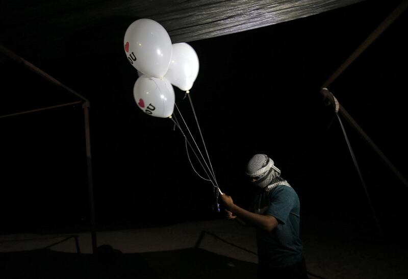 A masked Palestinian protester from a group calling themselves the "night confusion units" holds incendiary devices attached to ballons to be flown towards Israel, near the  Gaza-Israel border east of Rafah in the southern Gaza Strip.  AFP
