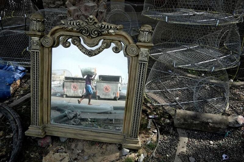 A discarded mirror reflects a fisherman as he loads his boat with a bait bag of bread in the Jumeirah 4 Harbour near Dubai Offshore Sailing Club.  Antonie Robertson  / The National