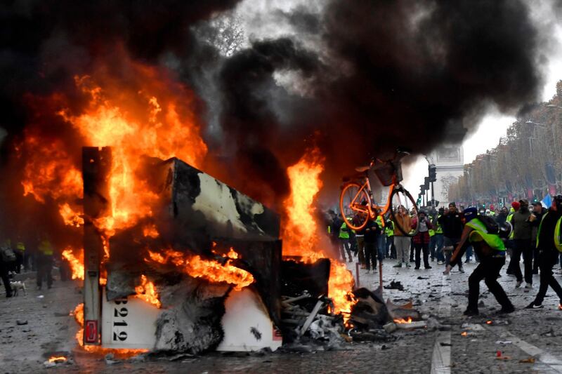 TOPSHOT - A man throws a bike in a burning truck during a protest of Yellow vests (Gilets jaunes) against rising oil prices and living costs near the Arc of Triomphe on the Champs Elysees in Paris, on November 24, 2018. 
 Police fired tear gas and water cannon on November 24 in central Paris against "yellow vest" protesters demanding French President Emmanuel Macron roll back tax hikes on motor fuel. / AFP / Bertrand GUAY
