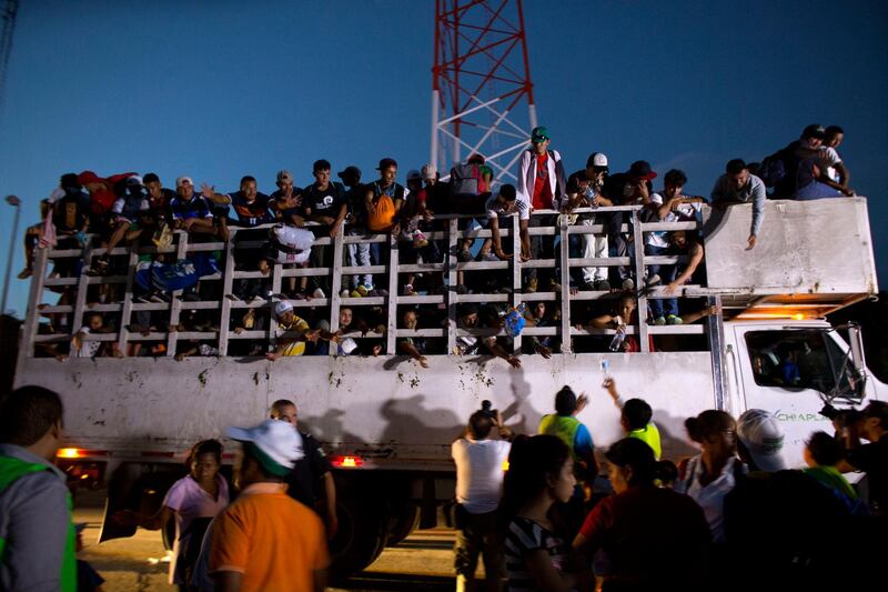 Men pass up water to Central Americans riding on the back of a truck while other migrants wait for rides, as a thousands-strong caravan of Central American makes its way toward the U.S. border, north of Pijijiapan, Mexico, at dawn on Friday, Oct. 26, 2018. Many migrants said they felt safer traveling and sleeping with several thousand strangers in unknown towns than hiring a smuggler or trying to make the trip alone.(AP Photo/Rebecca Blackwell)