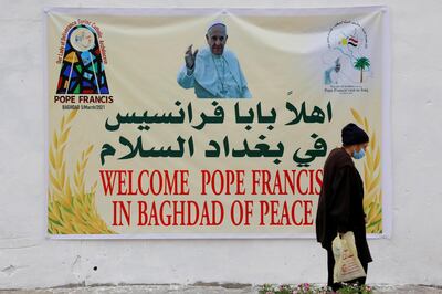 A woman walks near a poster of Pope Francis upon his upcoming visit to Iraq, in Baghdad, Iraq March 4, 2021. REUTERS/Teba Sadiq